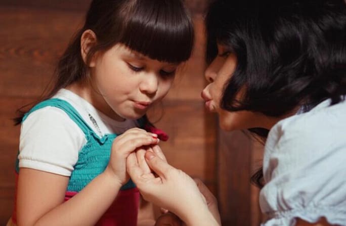 A woman helping a child dry her nail polish that was applied on her nails