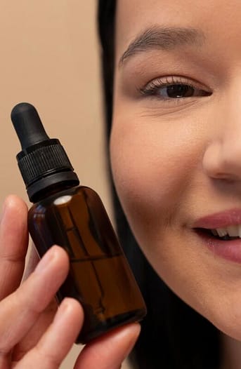 Woman holding close to her face a natural vitamin C Serum