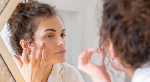 79A76BBF-49A8-456E-B8E1-6161E78EBF85 Women inspecting her face in a big mirror