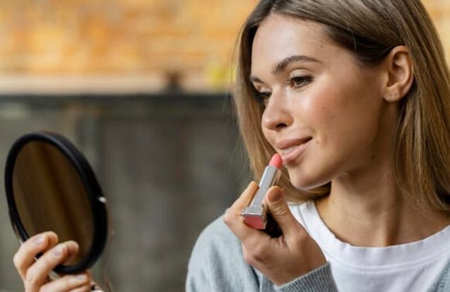 F4A89366-EC99-44D4-BF0C-55790BB90738 Woman applying lipstick while looking in a mirror