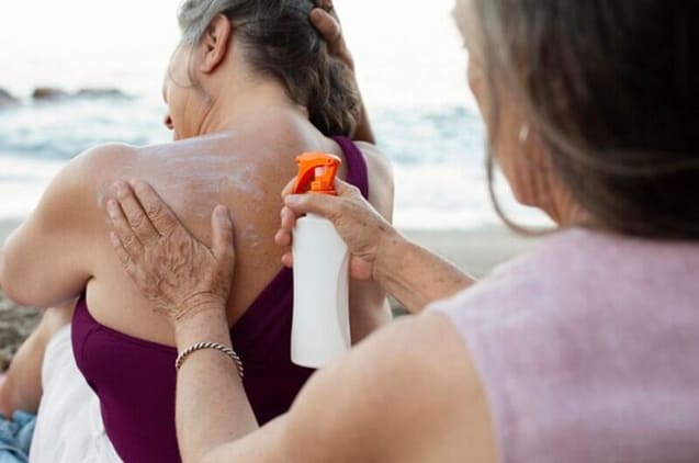 Two women helping eCh other out to make sure sunscreen is properly applied at their back.