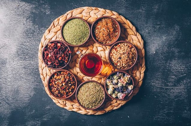 A470661E-ECAF-431A-A07D-6A8C9BF4ED7B A glass of tea surrounded by different tea leaves in bowls