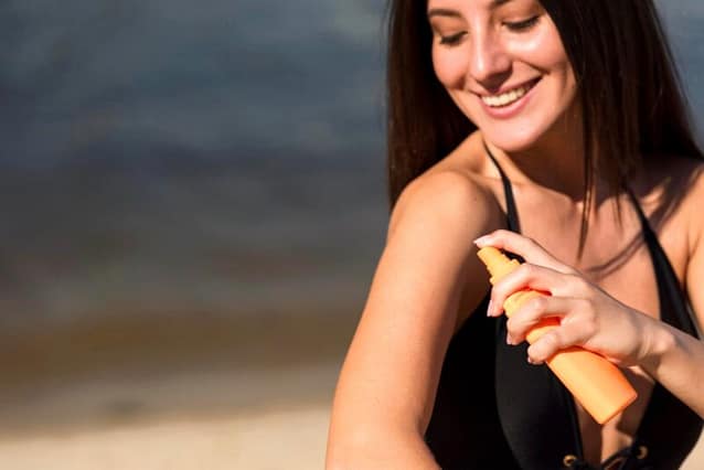 Happy woman in the beach using spray type sunscreen