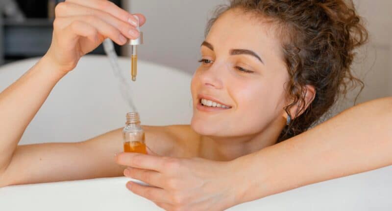 Woman in bath tub holding plant-based oil